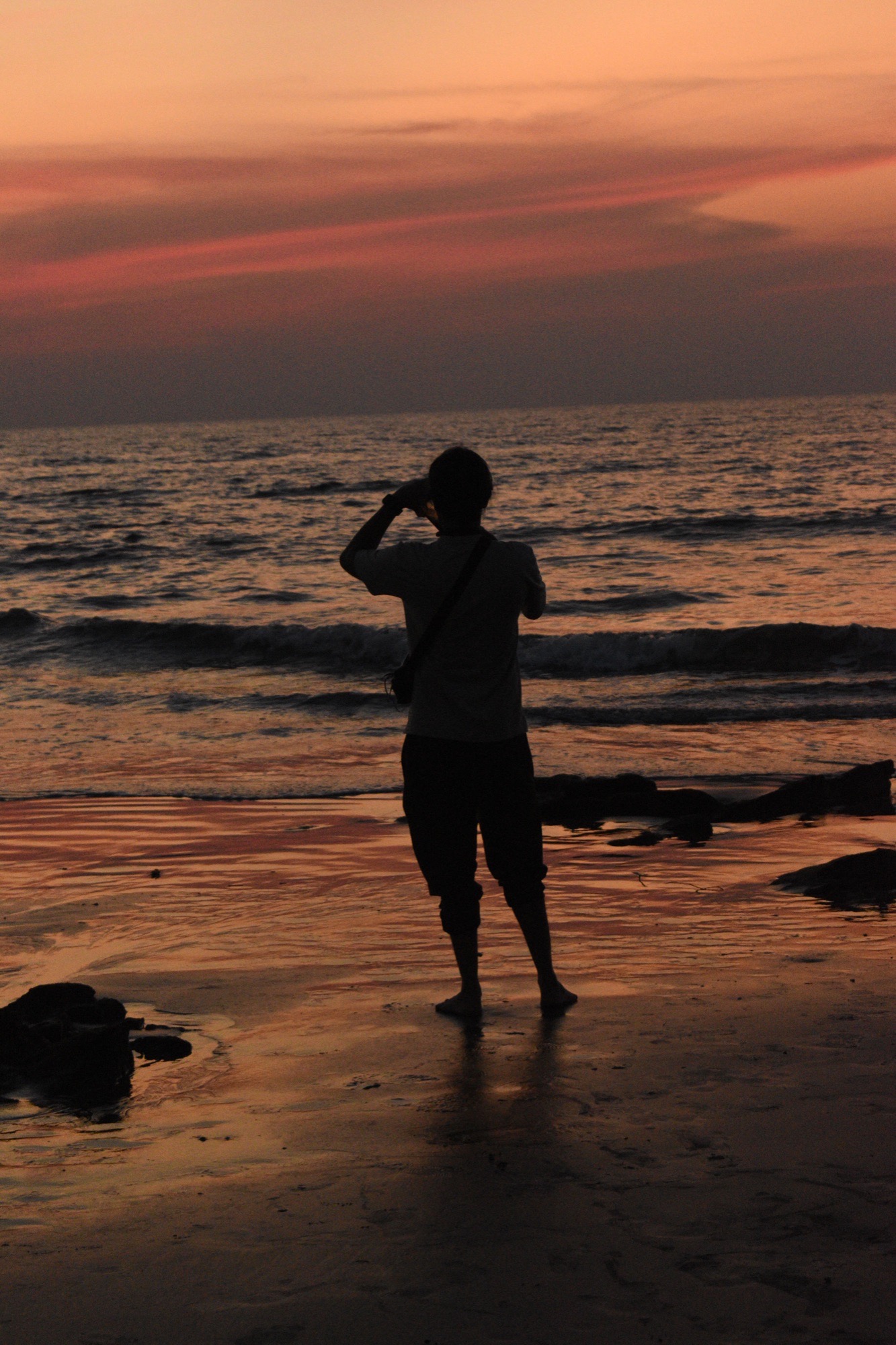 Figure crossing the sand at dusk with warm sunset tones reflecting on the wet beach