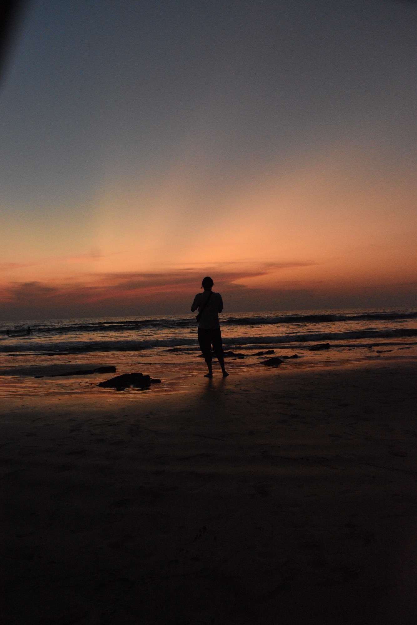 Lone silhouette on a wet beach beneath a peach-and-blue sunset sky