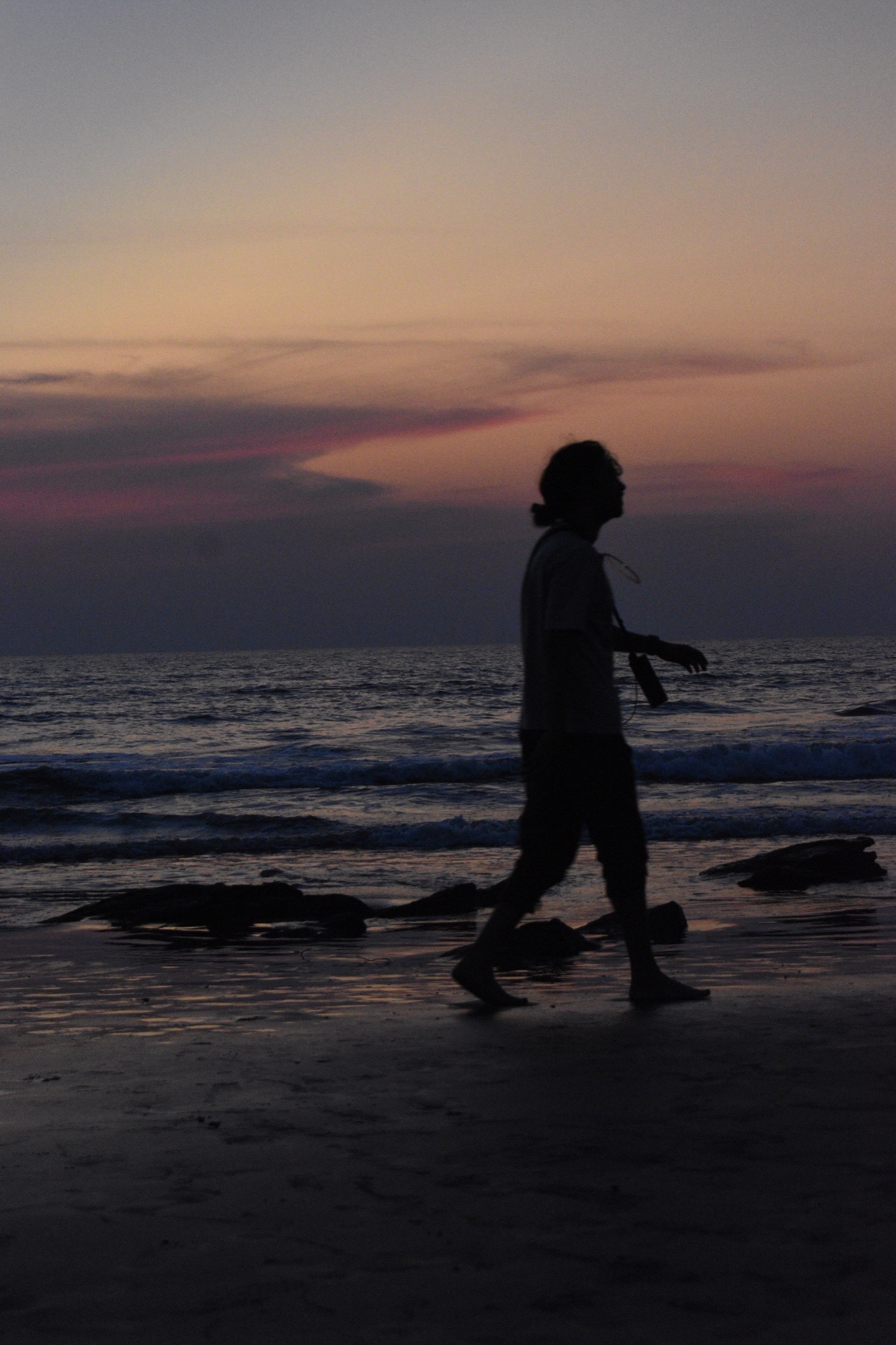 Silhouette walking along the shoreline as the sun sets over the sea